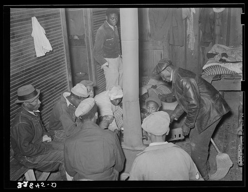 Group of Negro berry pickers huddled around the stove trying to keep warm on a cold day in the berry picking season. Near Independence, Louisiana