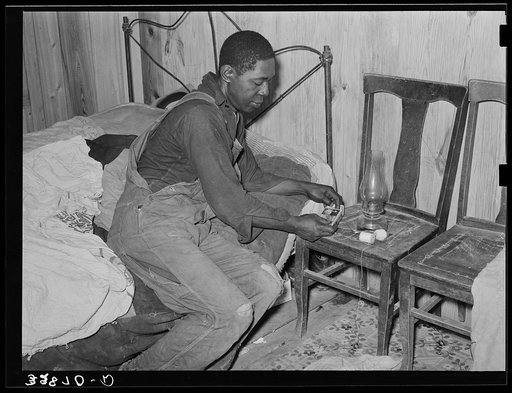 Negro man lighting lamp in bedroom of his home near Hammond, Louisiana. He works for a strawberry grower, doing odd jobs about the place