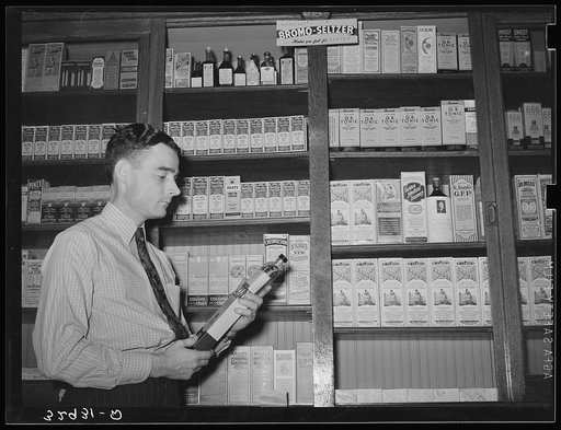 Druggist in front of patent medicine shelf. San Augustine, Texas