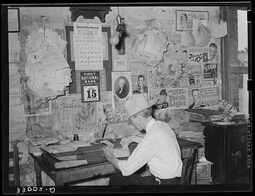 Small grocery store owner surrounded by bills. San Augustine, Texas