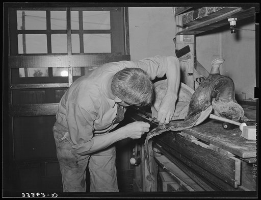 Saddle maker sewing saddle while repairing it. Saddle shop, Alpine, Texas