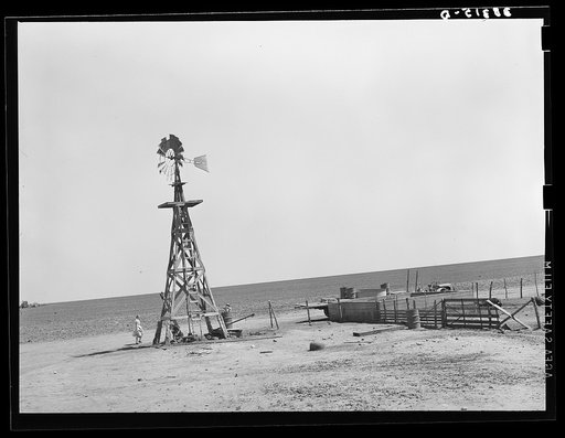 Windmill and watering trough on large farm near Ralls, Texas. Wife of day laborer is drawing water