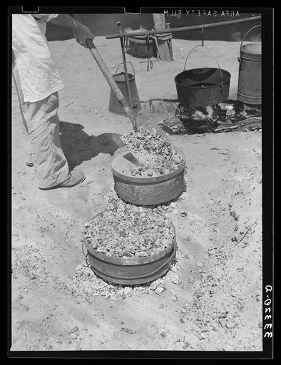 Piling coals on top of Dutch oven to bake bread. Ranch near Spur, Texas