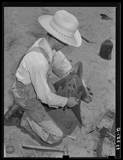 Day laborer adjusting plow point on tractor. Large farm near Ralls, Texas