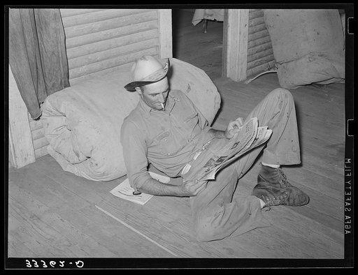 Cook of SMS Ranch propped against bedroll reading the paper. Bunkhouse on ranch near Spur, Texas