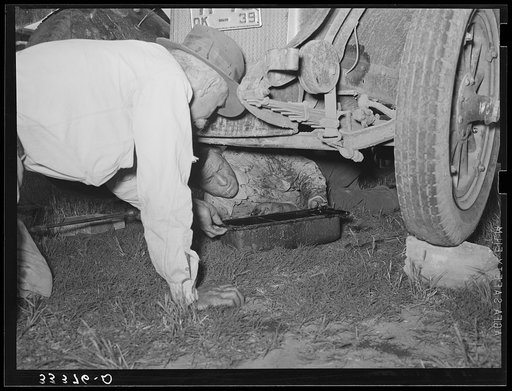 Migrant steeple-jack removing the crank case from his automobile. Near Prague, Oklahoma. When he secures a job, the entire family, consisting of his father and mother, wife and sister, all help with the painting