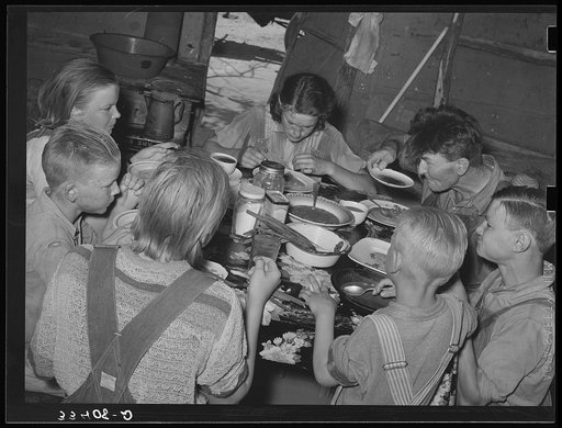 A family of agricultural day laborers eating dinner after a morning spent in chopping cotton. Though the fare of these people consists of the inexpensive and heavy starches, it is usually well prepared. This tent in which eight people lived was clean and neat. Notice the freshly combed hair of the y