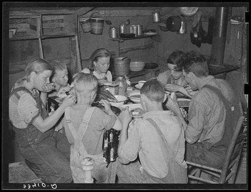 A family of agricultural day laborers eating dinner after a morning spent in chopping cotton. Though the fare of these people consist of the inexpensive and heavy starches, it is usually well prepared. This tent in which eight people lived was clean and neat. Notice the freshly combed hair of the yo