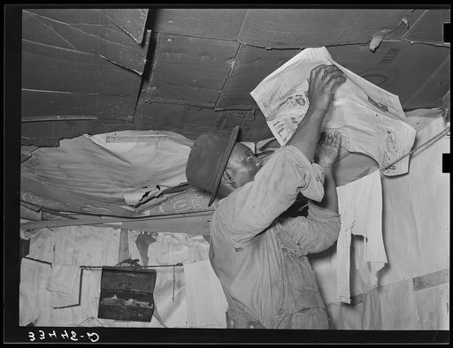Negro day laborer repapering his house. The wall and roof is in such bad condition that the house must be repapered every rain. Muskogee, Oklahoma