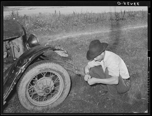 Untitled photo, possibly related to: White migrant squatting down in front of his automobile while camped near Prague, Olkahoma. These people use the term "hunkering down" instead of "squatting." "Hunkering down" is a slang term from the Indians