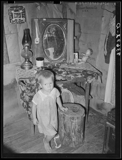 Child of agricultural day laborer in front of dressing table in shack. Near Vian, Oklahoma