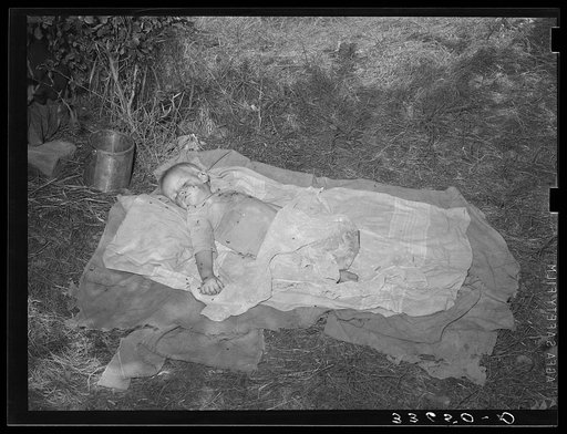 Baby of migrant agricultural day laborers asleep on the ground. There were no beds or cots in this camp near Spiro, Oklahoma. Sequoyah County