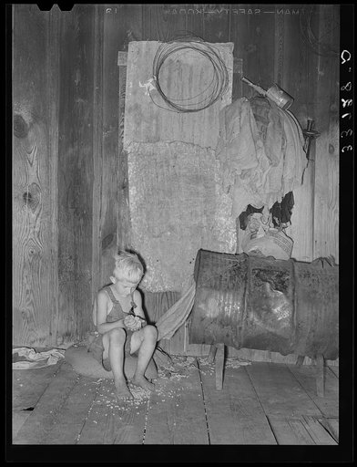 Son of agricultural day laborer examining cotton seed on front porch of home. Muskogee County, Oklahoma
