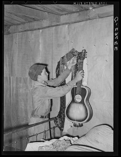Untitled photo, possibly related to: Migrant boy removing guitar before they leave for California. At old homestead near Muskogee, Oklahoma