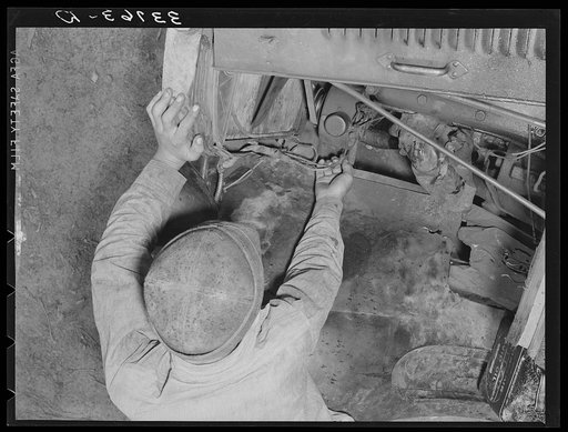 Migrant boy who is somewhat of a mechanic checking up the lighting wires of their improvised truck which will carry them to California. Near Muskogee, Oklahoma