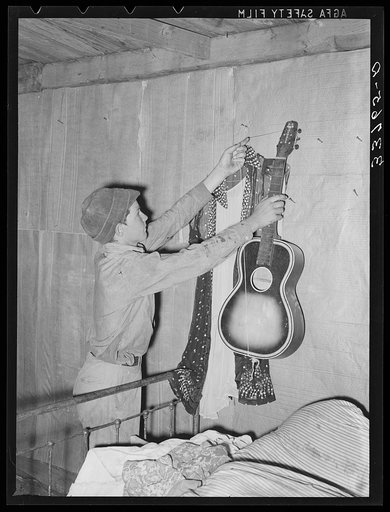 Migrant boy removing guitar before they leave for California. At old homestead near Muskogee, Oklahoma