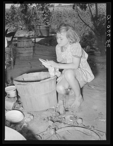 Daughter of migrant family wiping and packing dishes preparatory to leaving for California from Muskogee, Oklahoma