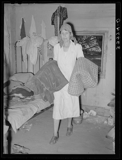 Mrs. Elmer Thomas, migrant to California, taking the blankets for packing into truck enroute to California from Muskogee, Oklahoma