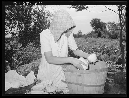 Packing dishes into bushel basket for transportation to California from Muskogee, Oklahoma. These people will become migrants