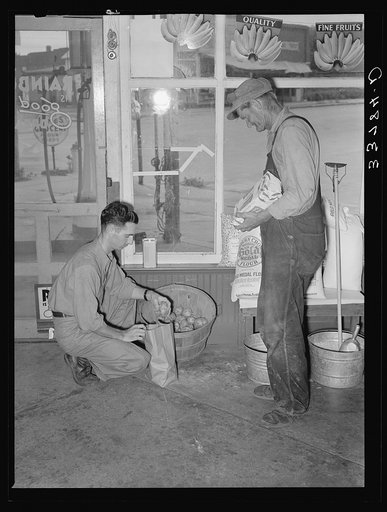 Migrant man stopped along the roadside in town to buy some potatoes which will form the basis for their noonday meal. Near Henryetta, Oklahoma