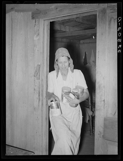 Mrs. Elmer Thomas, migrant to California, removing the spices, coffee, etc., to their car from their home which they are preparing to leave. Near Muskogee, Oklahoma