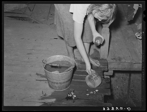 Daughter of tenant farmer living near Muskogee, Oklahoma, changing water in goldfish bowl. Refer to general caption number 20