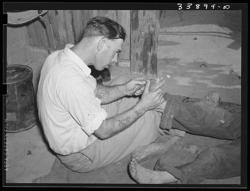 Resident of Mays Avenue camp taking out a piece of glass from boy's foot. Oklahoma City, Oklahoma