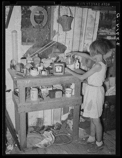 Child at cluttered table in shack home in Mays Avenue camp. Oklahoma City, Oklahoma. See general caption no. 21