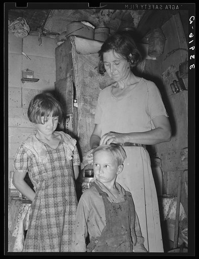 Woman in shack home in community camp. Oklahoma City, Oklahoma. Straightening her son's hair. Refer general caption no. 21