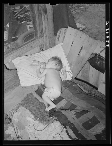 Baby with his bottle in shack home near Mays Avenue camp. Oklahoma City, Oklahoma. See general caption no. 21