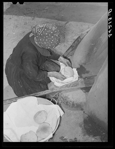Spanish-American woman removing freshly baked bread from outdoor earthen oven near Taos, New Mexico