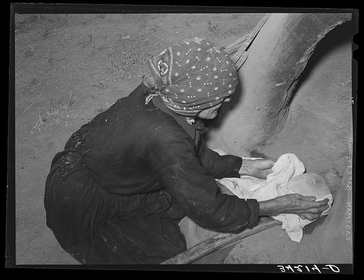 Spanish-American woman removing freshly baked bread from outdoor earthen oven near Taos, New Mexico