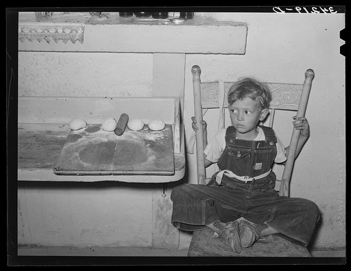 Spanish-American boy sitting in chair by tortilla board. Near Taos, New Mexico, Taos County