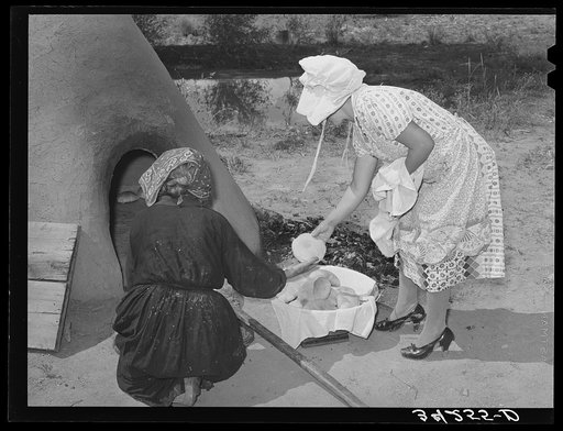 Wiping ashes from freshly-baked bread which has just been removed from earthen oven. Spanish-American farm home near Taos, New Mexico