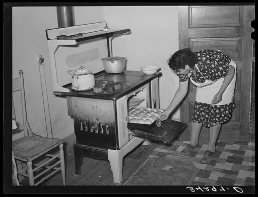 Spanish-American woman removing baked bread from oven farm near Taos, New Mexico