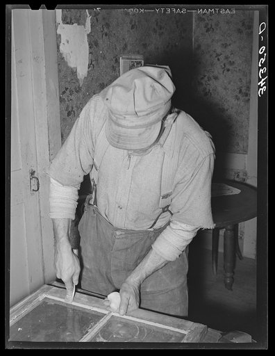 Farmer puttying a window. Farm near Bradford, Vermont. Orange County