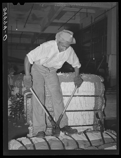 Snipping metal bands off bale of cotton before putting into compress. Houston, Texas