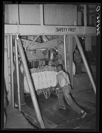 Placing bale of cotton into compressing unit. Compress, Houston, Texas. After going through the compress the bale of cotton is about one third its original size