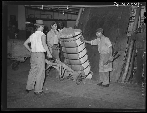 Guiding compressed bale of cotton onto hand truck. Compress, Houston, Texas