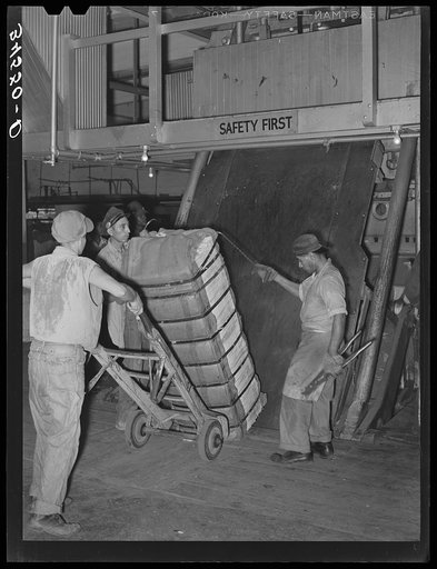 Guiding compressed bale of cotton onto hand truck. Compress, Houston, Texas