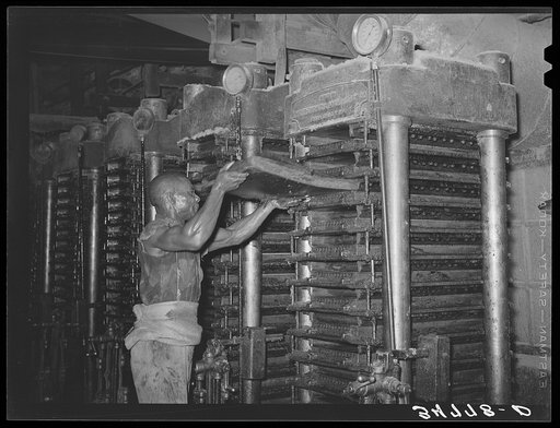 Negro workman inserting cotton seed filled mat into hydraulic press which will press out the oil and leave the cake. Cotton seed oil mill. McLennan County, Texas