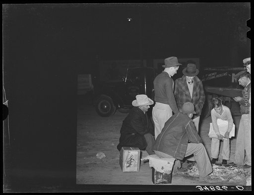 Group of men gathered around remains of fire at early morning vegetable market. San Angelo, Texas