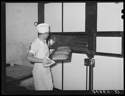 Removing tray of freshly baked bread from conveyor type oven. Bakery, San Angelo, Texas
