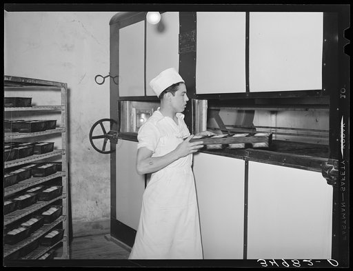 Putting loaves of bread into conveyor type oven for baking. Bakery, San Angelo, Texas