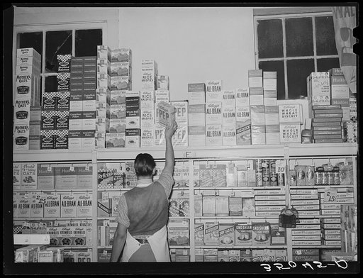 Placing packaged goods on display rack. Retail grocery, San Angelo, Texas