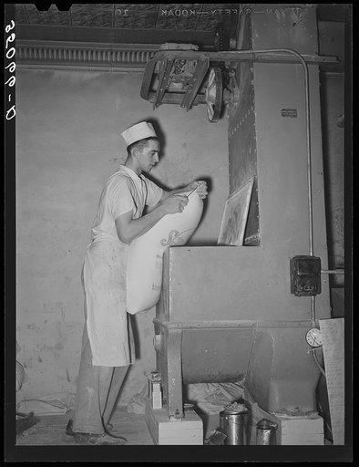 Emptying a sack of flour into the dough mixing machine. Bakery, San Angelo, Texas