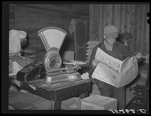Farmer reading newspaper in feed and general produce store. Eufaula, Oklahoma