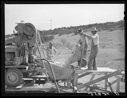 Road workers pouring gravel into concrete mixer. Menard County, Texas