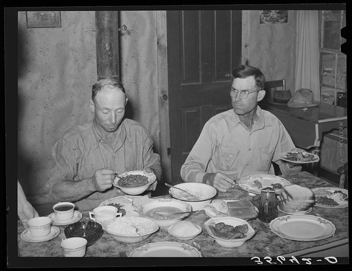 Dinner in the home of a rehabilitation borrower during goat shearing and kidding season. Man on the right is rehabilitation borrower and the one on the left is neighboring rancher who has been hired to help out with this seasonal work