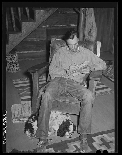 Manager of the Navajo Lodge working a crossword puzzle with his dog at his feet. Datil, New Mexico